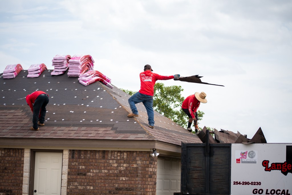 people with Lange Roofing throwing old shingles into trash bin